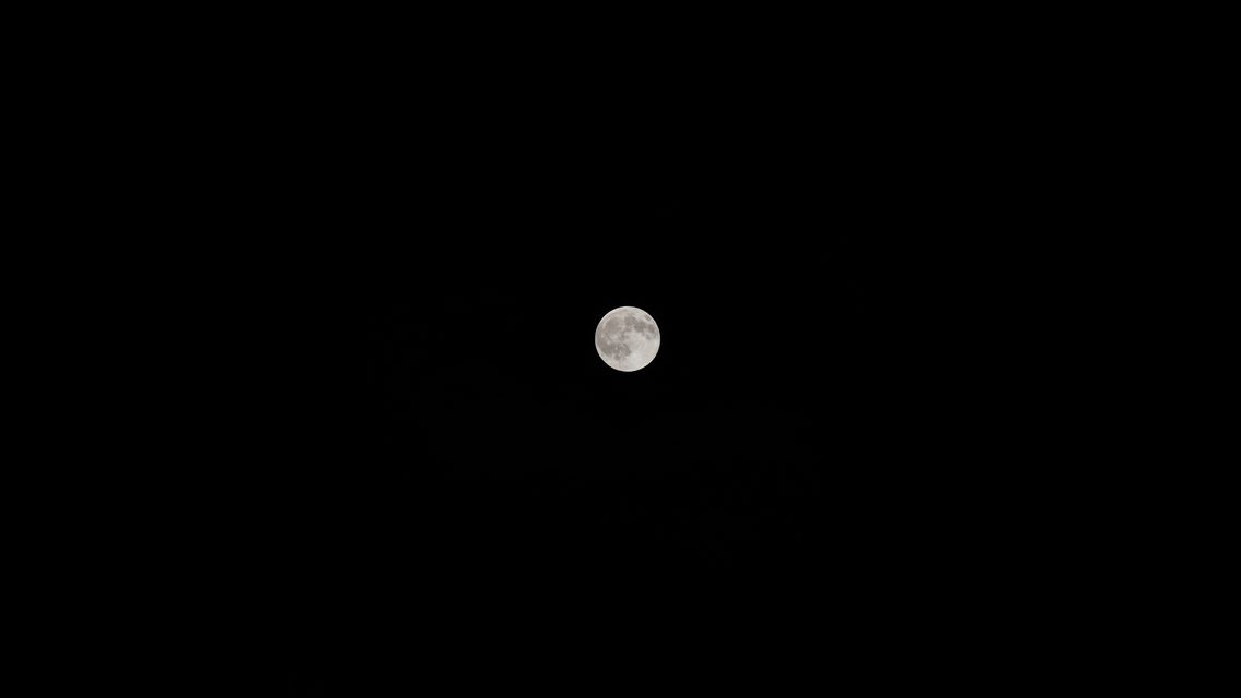 The full moon, small and bright in a black sky