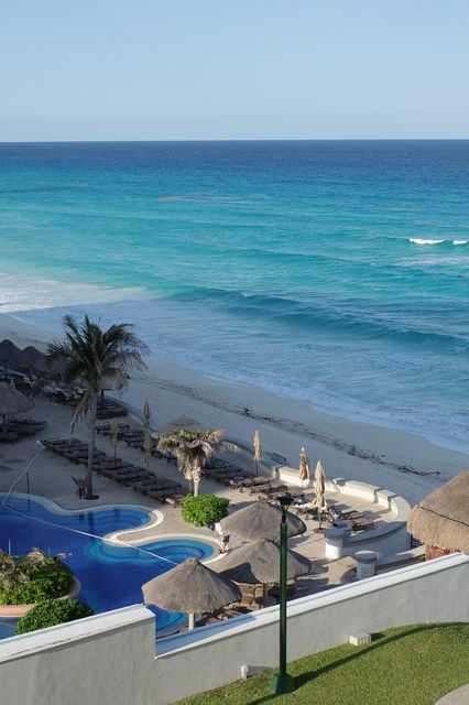 Turquoise sea and a resort pool with thatched umbrellas, seen from above
