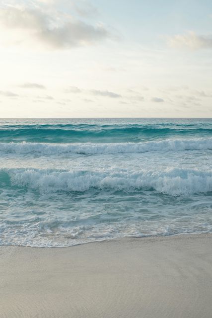 Waves breaking on an empty sandy beach under a pale sky
