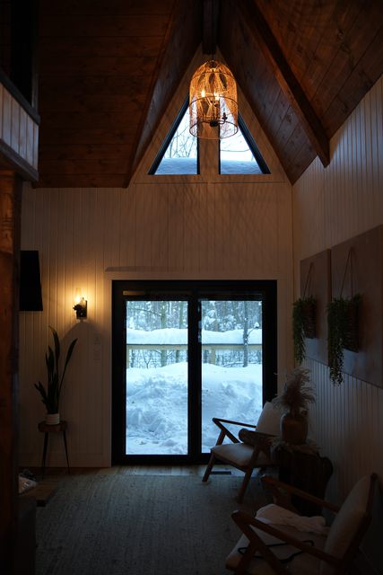 A wood-panelled A-frame cabin interior with a glass door onto snow