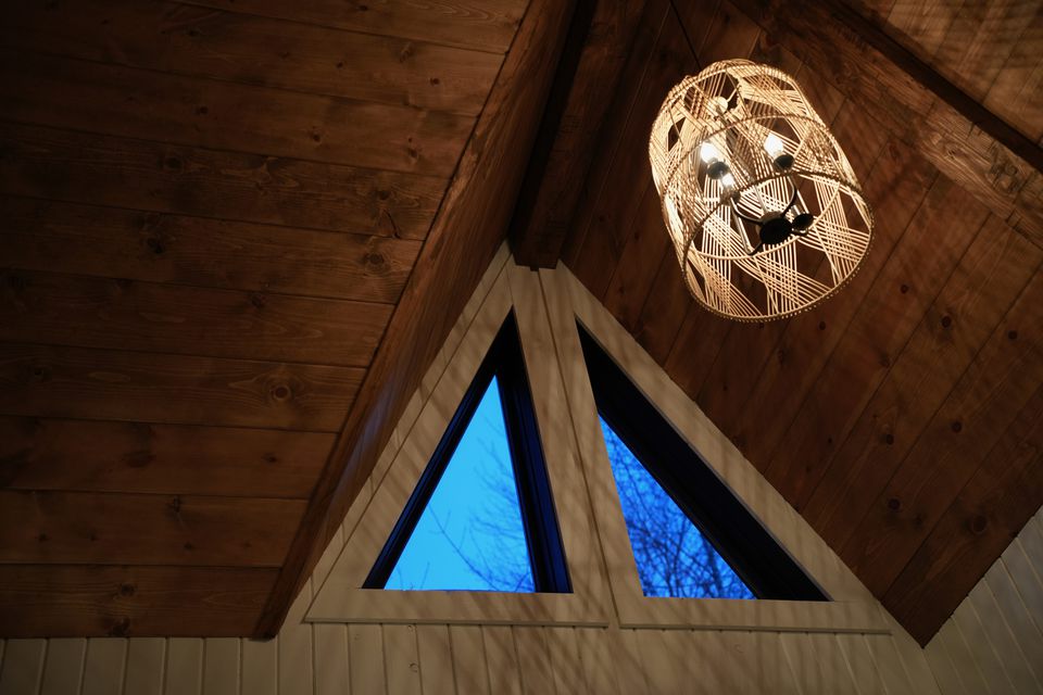 A woven pendant lamp under a timber ceiling, blue dusk in the triangular windows