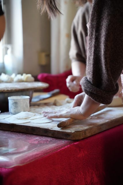 Hands rolling out dumpling wrappers on a floured wooden board