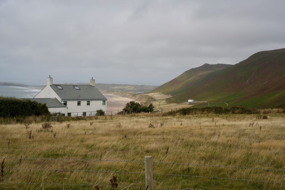 A white house on a grassy headland above a wide beach under heavy cloud