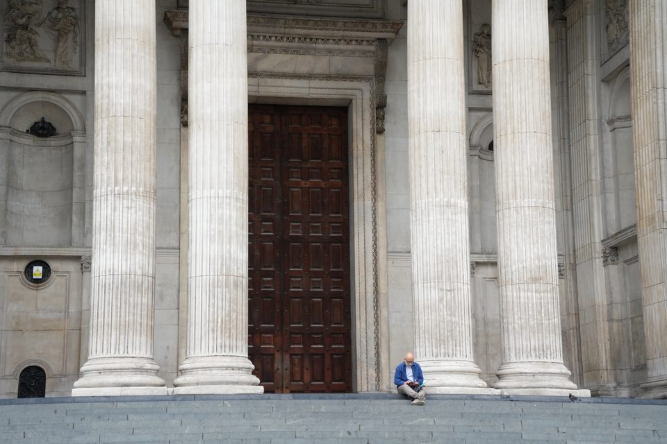 A man sitting alone on steps beneath tall stone columns and a wooden door