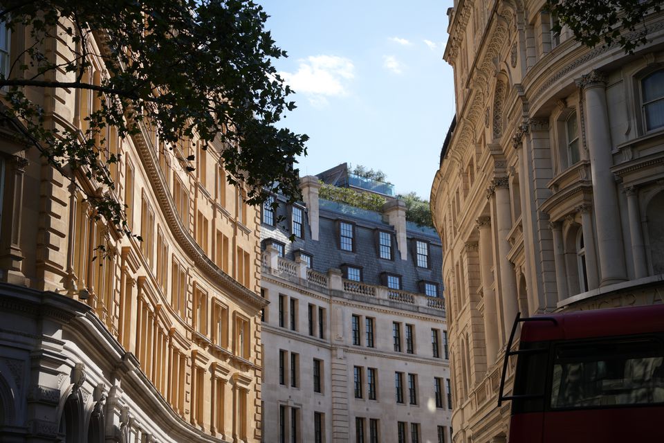 Curved stone facades in afternoon light, the top of a red bus below