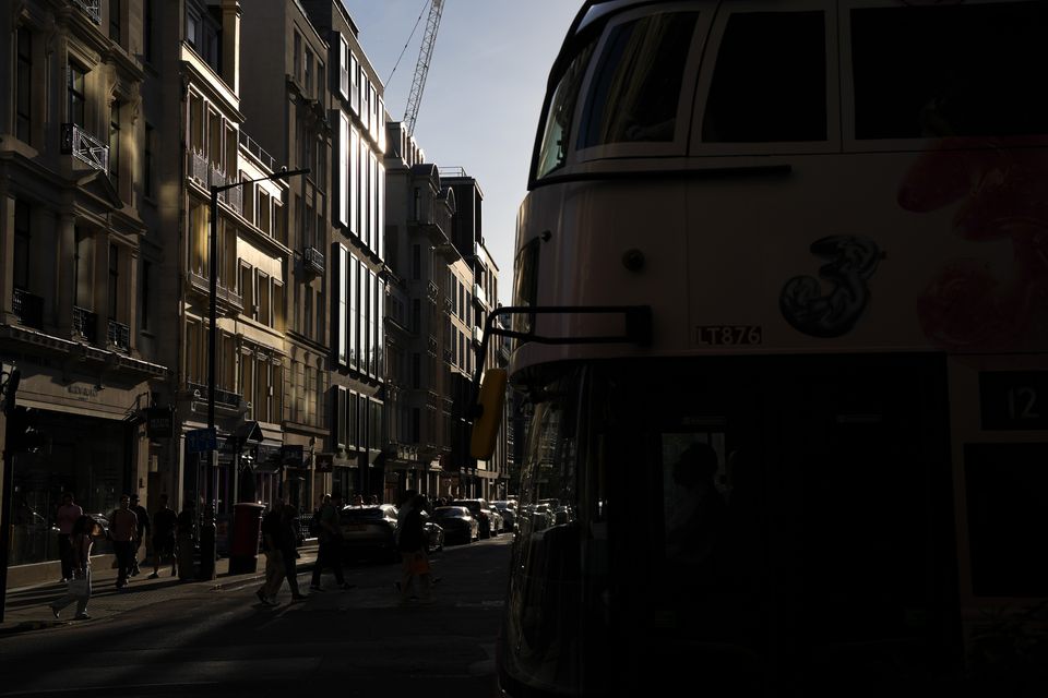 A vintage bus in shadow beside a street of tall stone buildings