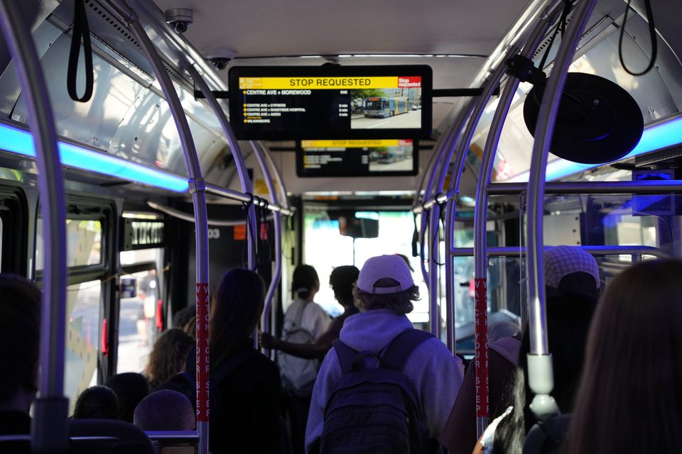Passengers standing inside a city bus lit in blue, a stop-requested sign overhead