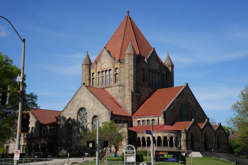 A sandstone church with red tiled roofs and a pointed tower under a blue sky