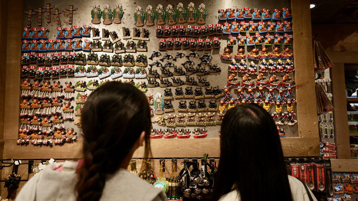Two people seen from behind looking at a wall of colorful souvenir magnets