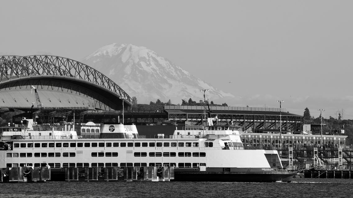 Black and white: a ferry in front of a stadium with Mount Rainier rising behind