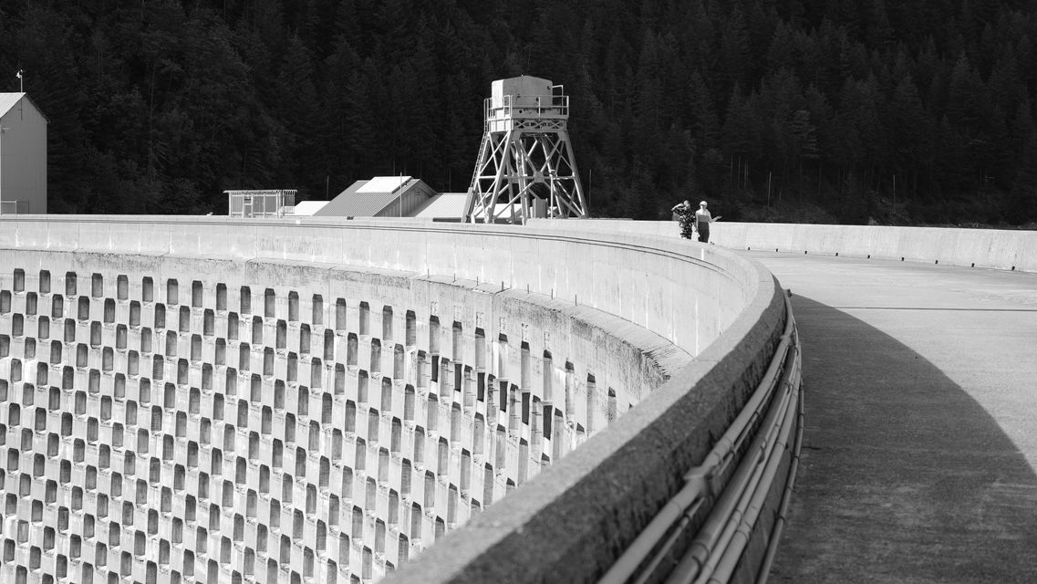 Black and white: two people walking along the curved top of a concrete dam