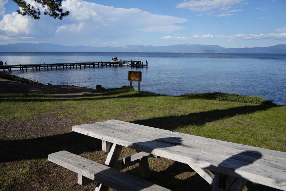 A weathered picnic table on a lakeshore with a wooden pier and mountains beyond