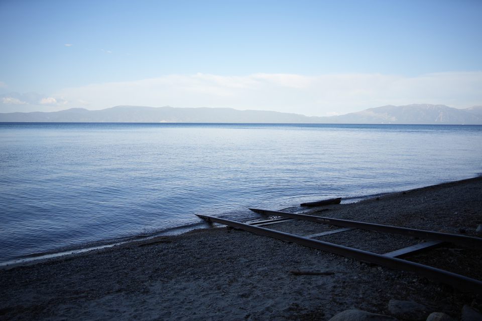 Old boat-launch rails running from a pebble beach into a still blue lake